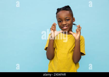 Hoffnungsvoller afroamerikanischer kleiner Junge, der mit gekreuzten Fingern steht Stockfoto