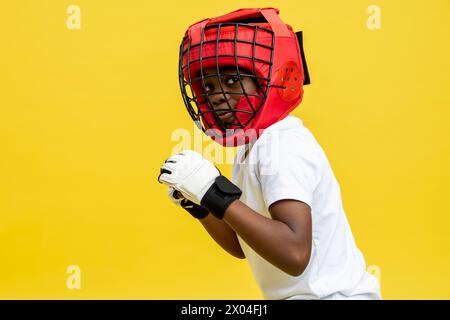 Dunkelhäutiger kleiner Boxkämpfer in Boxschutzhelm und -Handschuhen Stockfoto