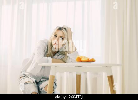 Eine Frau sitzt an einem Tisch mit einem Teller Persimmonen vor sich. Stockfoto