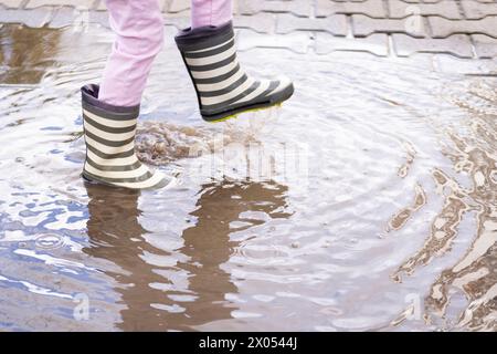 Nahaufnahme schelmiges 5-jähriges Mädchen springt freudig in die Pfütze, trägt Gummistiefel, Kinderfüße in Spritzwasser, springt glücklich, Freuden von ch Stockfoto