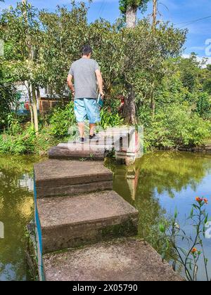 Erwachsene Männer nähern sich einer rustikalen Holzbrücke über einen ruhigen Teich, umgeben von üppigem Grün Stockfoto