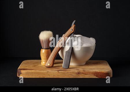 Klassische Rasierausrüstung mit Rasierer, Pinsel und Seife auf Holzständer vor dunklem Hintergrund Stockfoto