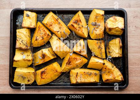 Im Ofen gebratener Butternusskürbis auf einer schwarzen Backform mit frischem Thymian und Salbei Kräutern in natürlichem Licht. Stockfoto