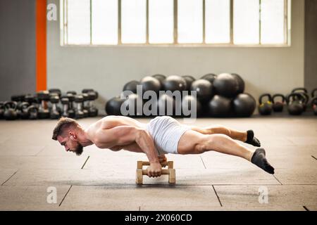 Der ganze Körper aus muskulösen Männchen in weißen Shorts mit Handstand blockiert die Dehnung des Körpers, während er während des Funktionstrainings im Fitnessstudio nach unten zeigt Stockfoto