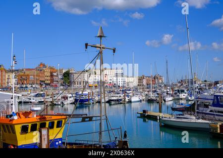 Ramsgate Royal Harbour voller verschiedener Boote und Yachten, unter einem blauen Himmel mit flauschigen weißen Wolken. Häuser im Hintergrund. Stockfoto