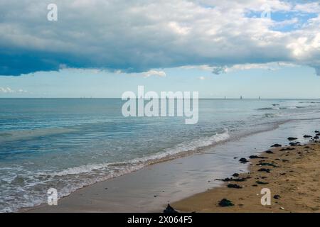 Ruhiger Strand mit ruhigem Meer unter dunklen, stürmischen Wolken. Tiefblaues Wasser, sanft über die Sandküste. Stockfoto