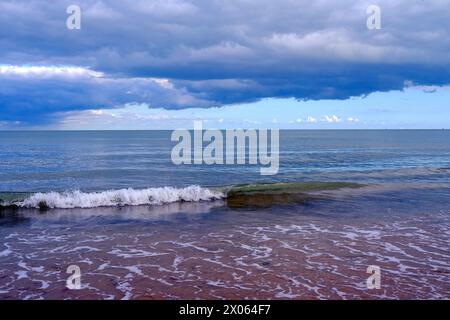 Ruhiger Strand mit ruhigem Meer unter dunklen, stürmischen Wolken. Tiefblaues Wasser, sanft über die Sandküste. Stockfoto