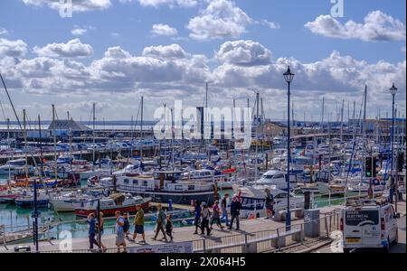 Ramsgate Royal Harbour voller verschiedener Boote und Yachten, unter einem blauen Himmel mit flauschigen weißen Wolken. Leute, die auf dem Dock laufen. Stockfoto