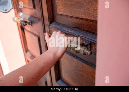 Eine Holztür und eine Hand auf einem massiven Metallgriff. Die Hand einer Frau öffnet oder schließt die Tür. Nahaufnahme. Stockfoto
