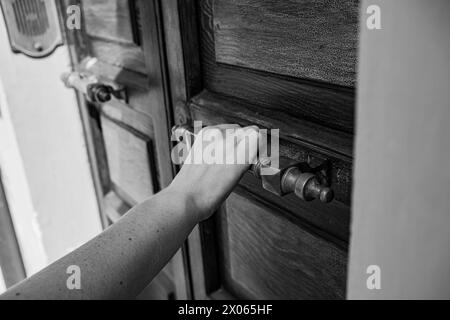 Eine Holztür und eine Hand auf einem massiven Metallgriff. Die Hand einer Frau öffnet oder schließt die Tür. Nahaufnahme. Stockfoto