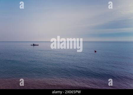 Meer, Ruhe, ein einsames Fischerboot am Ufer und eine rote Boje. Ein klarer Morgenhimmel, eine glatte, leicht kräuselnde Oberfläche aus Meerwasser, eine Ruhe und Erbsen Stockfoto