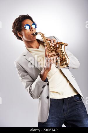 Mode, Sonnenbrille und Mann mit Saxophon im Studio mit klassischem, trendigem und stilvollem Outfit. Stil, gutaussehender und männlicher Musiker, der Blasmusik spielt Stockfoto