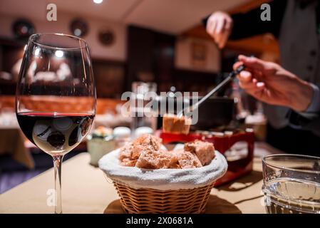 Intime Speiseszene mit Rotweinglas und Fonduekanne in gemütlicher Restaurantumgebung Stockfoto