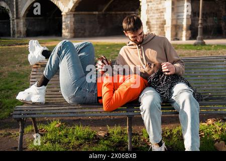 Multiethnische Paare teilen sich einen zärtlichen Austausch und entspannen auf einer Parkbank - romantische multikulturelle junge Erwachsene im intimen Moment, die sich in der Wärme o erfreuen Stockfoto