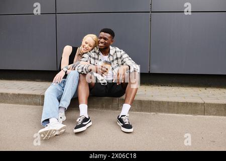 Ein Mann und eine Frau sitzen friedlich auf dem Boden bei einem grauen Gebäude in einer urbanen Umgebung und genießen einander Gesellschaft. Stockfoto