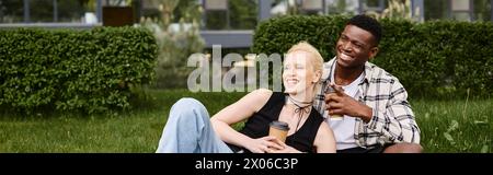 Ein glücklicher afroamerikanischer Mann und eine kaukasische Frau sitzen zusammen auf Gras im Park und schaffen ein Bild von fröhlicher Zweisamkeit. Stockfoto