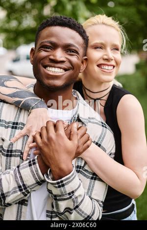 Ein glückliches multikulturelles Paar - ein Afroamerikaner, der eine kaukasische Frau in den Armen hält - in einer romantischen Umarmung draußen in einem Park. Stockfoto