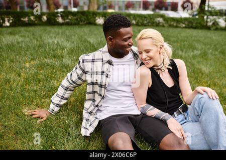 Ein glückliches, multikulturelles Paar, bestehend aus einem Afroamerikaner und einer Kaukasierin, die auf dem Gras in einem Park sitzt. Stockfoto