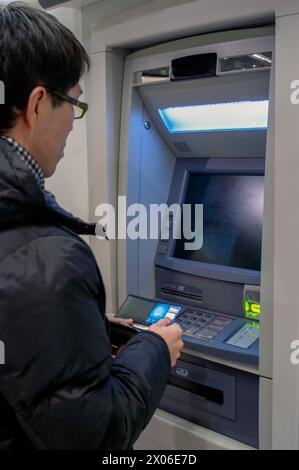 Porträt, junger asiatischer Mann von hinten, der Bargeld von der Geldautomat bei der Bank mit Kreditkarte abhebt. Stockfoto