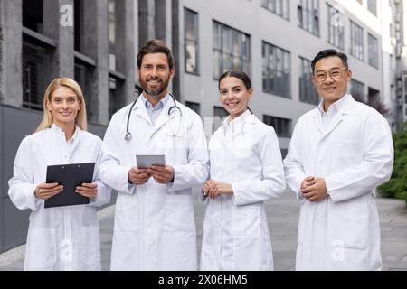 Eine Gruppe lächelnder junger interethnischer Männer und Frauen, Ärzte, Wissenschaftler und Studenten, die vor einem Gebäude stehen und in die Kamera lächeln. Stockfoto