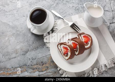 schweizer Schokoladen-Rollkuchen mit Erdbeeren und Frischkäse-Nahaufnahme auf einem Teller auf einem Marmorhintergrund. Horizontale Draufsicht von oben Stockfoto