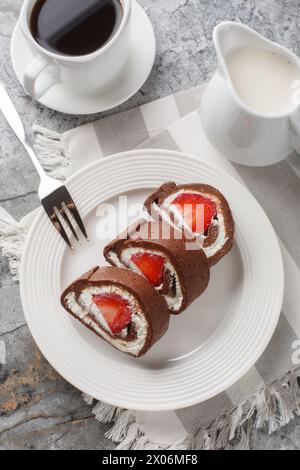 Erdbeerschokolade Schweizer Brötchen Käsekuchen serviert mit Kaffee in Nahaufnahme auf dem Tisch. Vertikale Draufsicht von oben Stockfoto