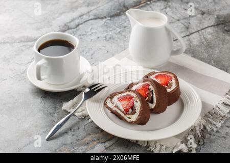 schweizer Schokoladen-Rollkuchen mit Erdbeeren und Frischkäse-Nahaufnahme auf einem Teller auf einem Marmorhintergrund. Horizontal Stockfoto