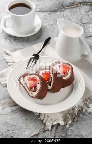 Erdbeerschokolade Schweizer Brötchen Käsekuchen serviert mit Kaffee in Nahaufnahme auf dem Tisch. Vertikal Stockfoto