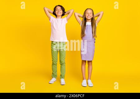 Foto in voller Länge von positiven träumenden Freunden tragen legere Outfits Arme hinter Köpfen isolierter gelber Hintergrund Stockfoto