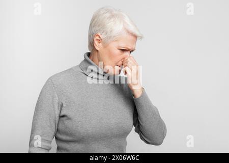 Ältere Frau, die mit geschlossener Nase auf grauem Hintergrund steht Stockfoto
