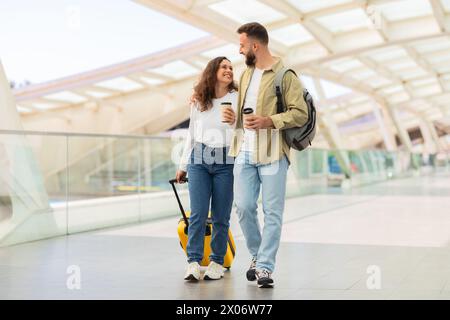 Mann und Frau gehen durch den Flughafen mit Gepäck und Kaffee zum Mitnehmen Stockfoto