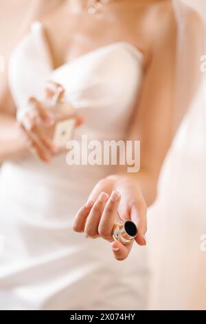 Eine wunderschöne Braut in stilvollem Hochzeitskleid sprüht Parfüm auf sich. Frau steht im Badezimmer Stockfoto