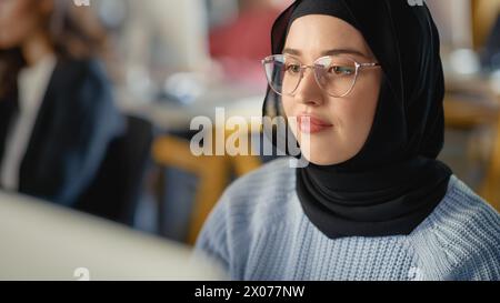 Wunderschönes Porträt einer muslimischen Studentin in Hijab, die an der Universität studiert. Sie arbeitet am Desktop-Computer im College. Ihr Wissen anwenden, um akademische Fähigkeiten im High School Classroom zu erwerben. Stockfoto