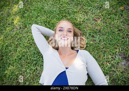 Eine lächelnde junge Frau liegt mit ausgebreiteten Armen auf dem Gras. Stockfoto