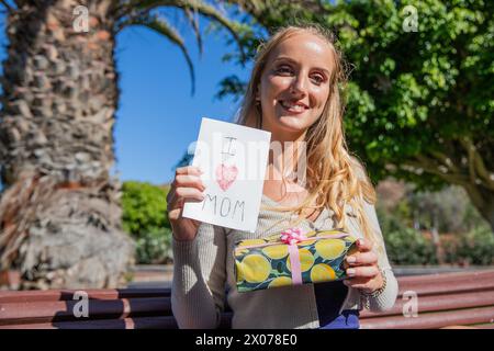 Eine Frau, die eine Karte mit der Aufschrift „Ich liebe dich Mom“ hält und ein Geschenkgeschenk, Muttertagsfeier. Stockfoto