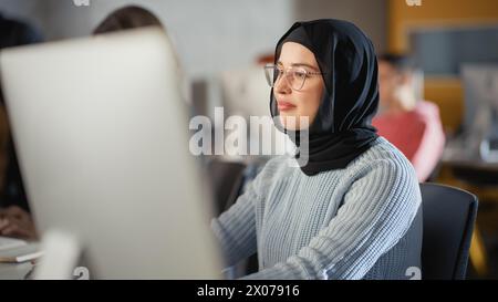 Wunderschönes Porträt einer muslimischen Studentin in Hijab, die an der Universität studiert. Sie arbeitet am Desktop-Computer im College. Ihr Wissen anwenden, um akademische Fähigkeiten im High School Classroom zu erwerben. Stockfoto