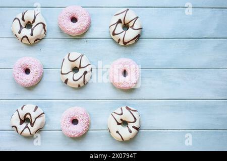 Flatlay von gefrosteten Vanilledonuts mit Schokoladenstrudel und rosa Donuts mit Kokosflocken mit Kopierraum. Draufsicht von oben. Stockfoto