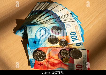 Ein Stapel Geld, hundert Scheine, 20 Münzen, auf einem sonnendurchfluteten Holztisch mit Schattenlinien vom Fenster. Schweizer Währung. Stockfoto