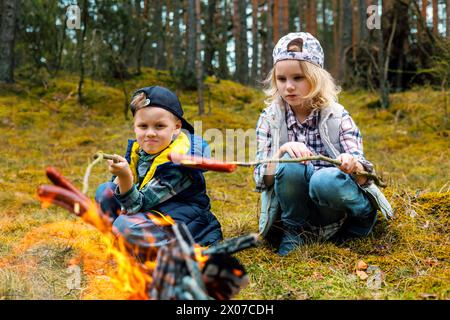 Kinder braten Würstchen auf Spießen über einem Lagerfeuer im Wald. Camping mit Kindern. Sommercamp Stockfoto