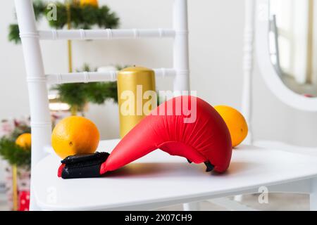 Sportausrüstung: Kurzhantel, Boxhandschuhe, Tannenzweig, Weihnachtsschmuck, Geschenke auf Stuhl. Stockfoto