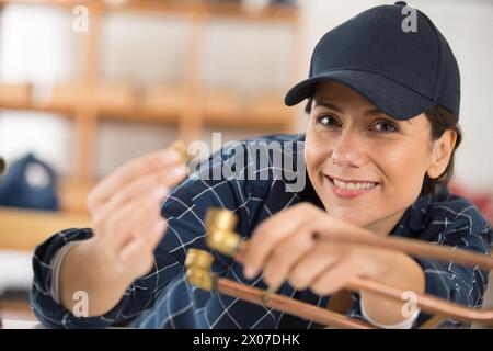 Glückliche Klempnerin, die im Haus mit cooper Rohren arbeitet Stockfoto