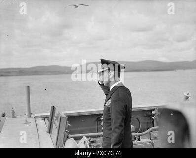 DER KÖNIG BESUCHT DIE HEIMATFLOTTE. 15. AUGUST 1943, SCAPA FLOW. DER KÖNIG BESUCHTE MÄNNER UND SCHIFFE DER HEIMATFLOTTE, ER GING AN BORD DES FLOTTENFÜHRERS HMS ONSLOW, DER IHN ZUM FLAGGSCHIFF HMS DUKE OF YORK BRACHTE. HIER TRAF DER KÖNIG AUF ADMIRAL SIR BRUCE A FRASER, KBE, CB, C-IN-C-FLOTTE. - Der König auf der Brücke der HMS PHOEBE salutiert das Flaggschiff Stockfoto