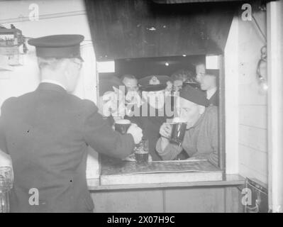 KREUZKANALDAMPFER JETZT ERHOLUNGSSCHIFF FÜR SEELEUTE. JUNI 1943, SCAPA FLOW. DER KREUZKANALDAMPFER AUTOCARRIER, DER FRÜHER URLAUBSWAGEN VON UND NACH FRANKREICH TRANSPORTIERTE, IST HEUTE EIN ERHOLUNGSSCHIFF FÜR DIE BESATZUNGEN DER VIELEN HILFSKRAFTSCHIFFE DER HEIMATFLOTTE, DIE SICH UM DEN SERVICE DER ROYAL NAVY KÜMMERN. ES IST DAS ERSTE UND EINZIGE SEINER ART, UND FÜR TAUSENDE VON MÄNNERN BEDEUTET ES EINMAL PRO WOCHE BIER UND "FLICKS". - Nach der Show strömen die Männer in die Bar, um einen wohlverdienten Drink zu trinken Stockfoto