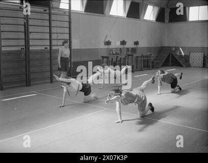 FABRIKWOHLFAHRT: WOHLFAHRT IN PILKINGTON'S GLASFABRIK, ST HELENS, LANCASHIRE, ENGLAND, VEREINIGTES KÖNIGREICH 1944 – Frauen machen Dehnungsübungen im Turnsaal im Rehabilitationszentrum der Fabrik (wahrscheinlich in Pilkington's Glaswerk in St Helens), um sich nach einer Verletzung zu erholen. Sie knien auf dem Boden, mit einem Bein und dem anderen Arm gestreckt. Der Originalüberschrift zufolge ist es das Ziel [des Zentrums], Männer und Frauen daran zu hindern, dauerhaft behindert zu werden. Durch Übungen und Massagen unter der Leitung eines in modernen Methoden ausgebildeten Physiotherapeuten die Verletzten Stockfoto