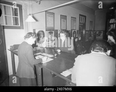 16-JÄHRIGE REGISTRIEREN SICH: TEENAGER ERHALTEN IHRE AUSWEISKARTEN FÜR ERWACHSENE AN DER ARBEITSBÖRSE in LONDON, ENGLAND, Großbritannien, 1945 - 16-jährige Margaret Neal, eine Schneiderassistentin, meldet sich bei der Islington Labour Exchange für ihren Ausweis für Erwachsene an. Laut der Originalüberschrift nimmt Margaret "keinen Abendunterricht, sie gehört auch keiner Jugendorganisation an und wird daher später von den Jugendbehörden befragt werden". Hinter ihr sind viele Rekrutierungsplakate zu sehen Stockfoto