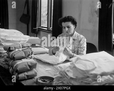 IN EINEM ADMIRALITÄT-BEKLEIDUNGSDEPOT. 17. OKTOBER 1944, MARINELAGER IM SÜDLICHEN GEBIET, GUILDFORD. OFFIZIERE, MÄNNER UND FRAUEN DER ROYAL NAVY WISSEN, DASS SIE EIN GUTES PREIS-LEISTUNGS-VERHÄLTNIS BEKOMMEN, WENN SIE IN DEN „PUSSERS STORES“ EINKAUFEN, DEM SPITZNAMEN DER NAVY FÜR DAS BEKLEIDUNGSDEPOT AN LAND ODER AUF SEE. JEDES KLEIDUNGSSTÜCK MUSS EINEN DOPPELTEN TEST BESTEHEN UND AUF QUALITÄT, GEWICHT UND DESIGNGENAUIGKEIT PRÜFEN, BEVOR ES DEN EIGENTLICHEN AUSSTELLUNGSRAUM FÜR KLEIDUNG ERREICHT. - Frau E Sloggatt, Schneiderin in Friedenszeiten, untersucht die Hemden der Beamten auf schlechte Nähte und Baumwollspitzen Stockfoto