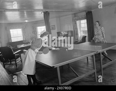 VILLA WIRD ENTBINDUNGSHEIM: LEBEN IN BROCKET HALL, WELWYN, HERTFORDSHIRE, 1942 - zwei Krankenschwestern (eine in Uniform, die andere in Zivilkleidung) spielen Tischtennis oder Tischtennis in ihrem Wohnzimmer nach einem anstrengenden Tag im ENTBINDUNGSHEIM Brocket Hall Stockfoto