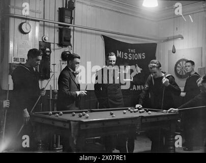 KAPLAN DER KIRCHE VON ENGLAND. 1940. OKTOBER: REVEREND S J GAMON, KAPLAN AUF DER MARINEBASIS GRIMSBY. - Der Kaplan auf der Uferbasis arbeitet eng mit den Seamen-Missionen zusammen. Hier ist er im Clubraum und beobachtet Männer der Patrouillenschiffe beim Billard Stockfoto