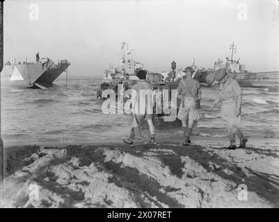 Während der Landung auf Sizilien am 9-10. Juli 1943 unterstützte ein Traktor ein gepanzertes Fahrzeug, das im Schlamm steckte, wobei mehrere Landungsfahrzeuge bei Sonnenaufgang sichtbar waren. Stockfoto