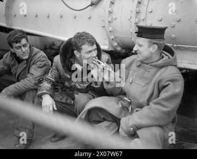 ROYAL NAVY RETTET AMERIKANER IN INVASION BAY. 9. JUNI 1944, AN BORD DES ZERSTÖRERS HMS BEAGLE, NACH EINEM DEUTSCHEN E-BOOT-TORPEDOANGRIFF AUF ZWEI AMERIKANISCHE LSI HMS BEAGLE VERJAGTE DIE ANGREIFER UND HALF, ÜBERLEBENDE VON DEN LSI ZU RETTEN - Ein US-Seemann, der von der HMS BEAGLE abgeholt wurde, bekommt ein Licht von einer britischen Bewertung, die ihn gerettet hat Stockfoto